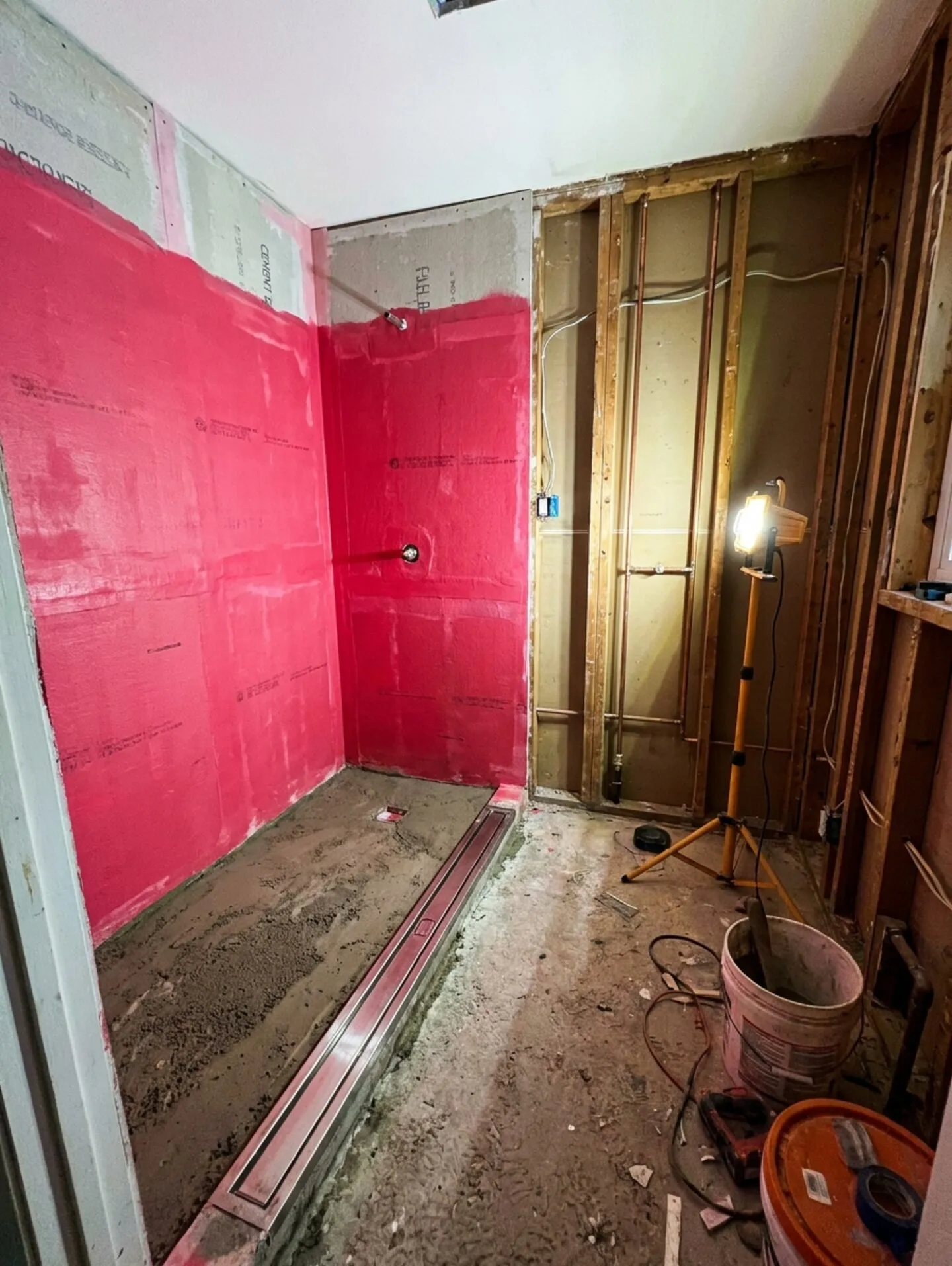 The same room mid-renovation: tanked and waterproofed shower zone with linear drain